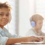 Foto: Shutterstock / AnnaStills. Bildet viser en gutt med datamaskin og hodetelefoner på skolen.