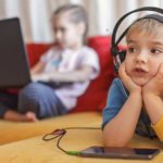 Foto: Shutterstock / Maria Symchych. Bildet viser to barn i en sofa, med mobiltelefon og PC.