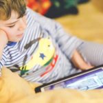 Foto: Shutterstock / Irina Wilhauk. Bildet viser en gutt som sitter i en sofa med et nettbrett i fanget.